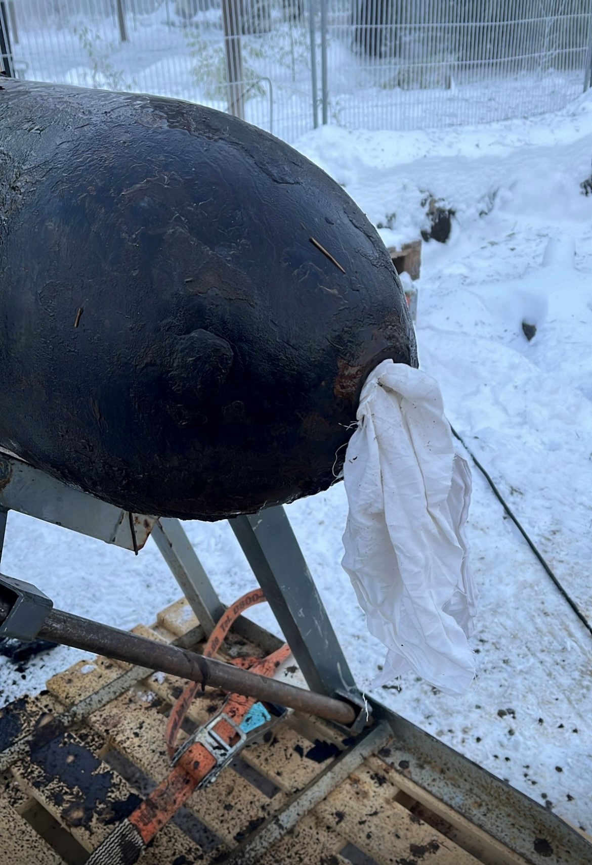 Nahaufnahme des entschärften Bombenzünders einer Weltkriegsbombe; aus der Öffnung ragt ein weißes Tuch, die Bombe liegt auf einer Metallhalterung im verschneiten Außenbereich.